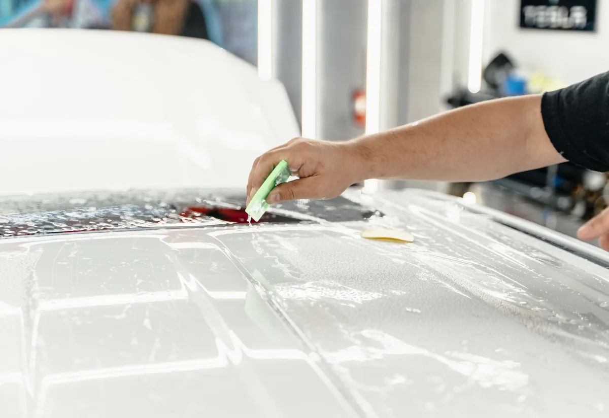 Gloss Clear PPF being smoothed on lower roof edge — inspection zone for edge lift