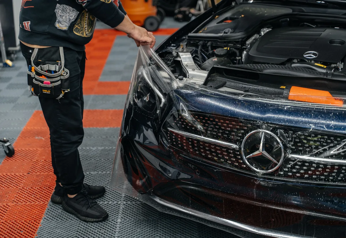 Hussle Customz installer finishing a STEK PPF edge on a Mercedes front bumper in Los Angeles