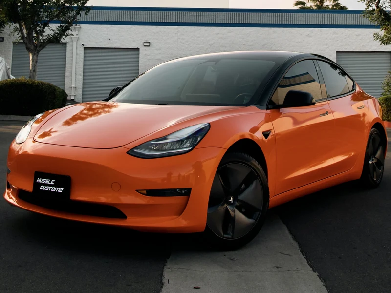 Tesla Model 3 wrapped in gloss orange vinyl by Hussle Customz Los Angeles — full color change install